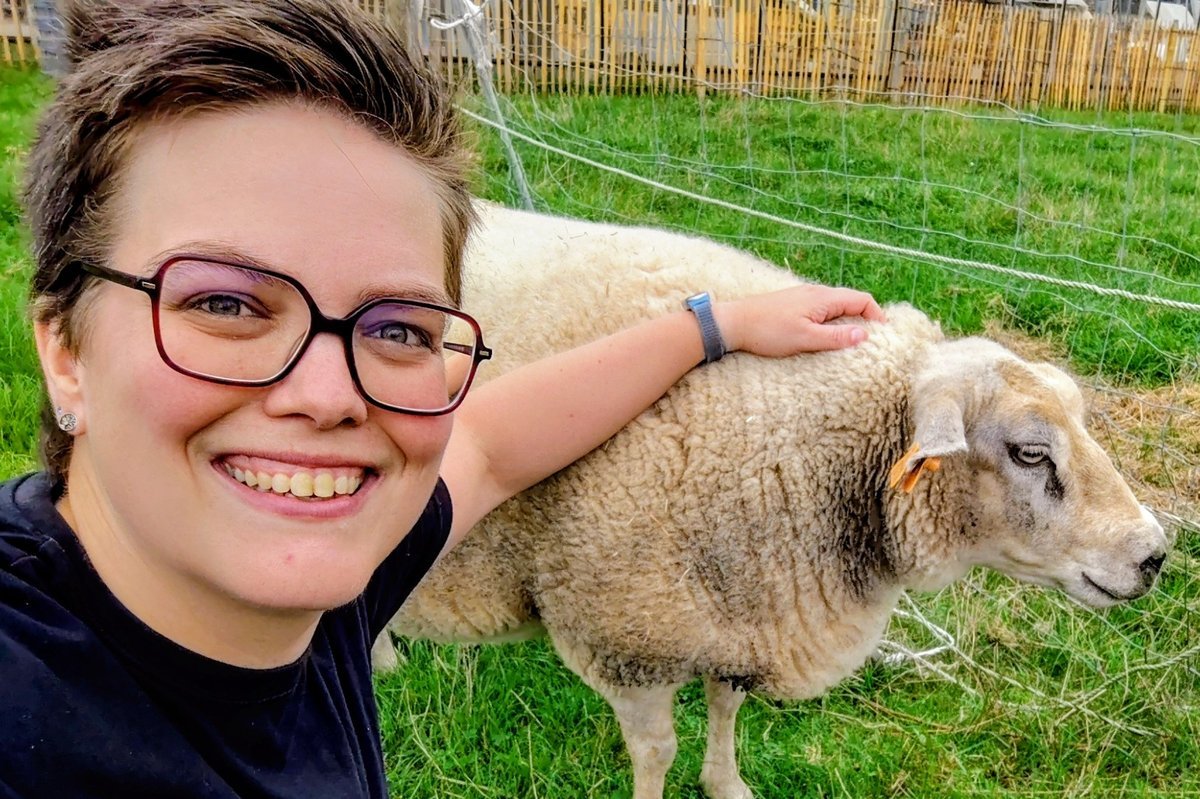 Cindy lachend in de wei, met haar hand op een schaap
